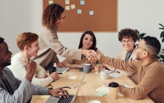 A group of men and women of various ages and ethnicities sit around a meeting table.