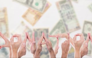 The word donation spelled out using human hands in front of different currencies.