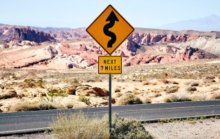 A road sign with a winding road symbol that says "Next ? Miles"