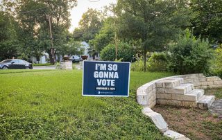 Blue campaign yard sign with white letters, on a lawn, saying "I'm So Gonna Vote."
